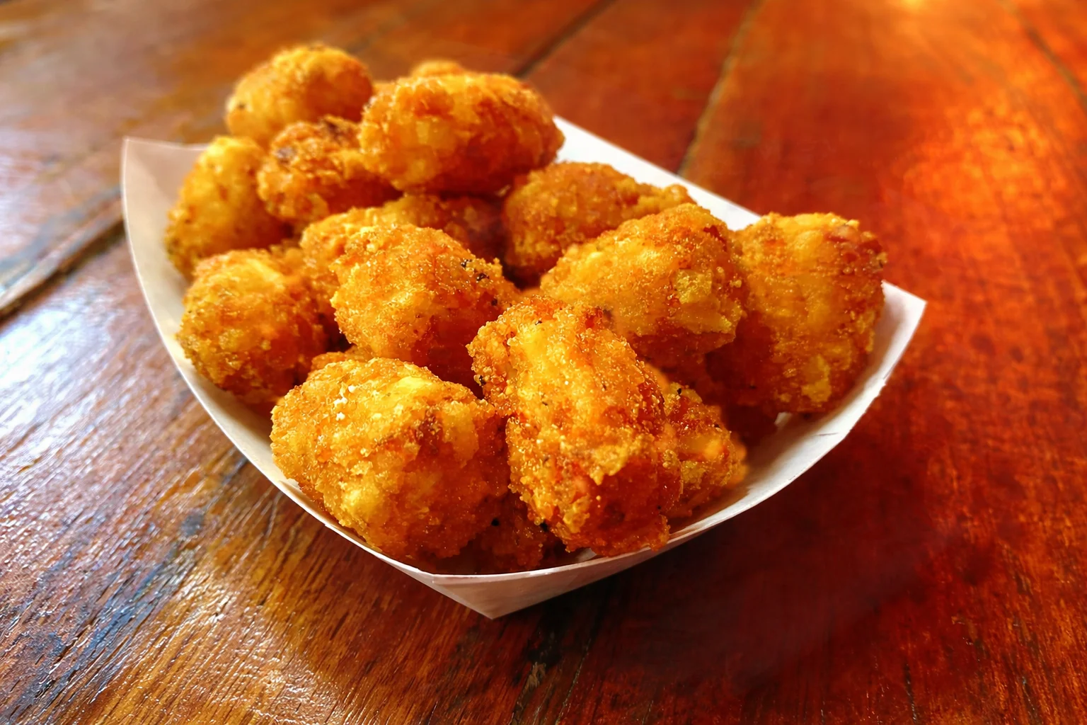 Crispy golden tots in a paper tray on a wooden table